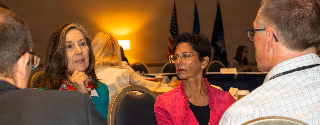 Elizabeth Orona in conversation with community leaders around a table at a regional meeting